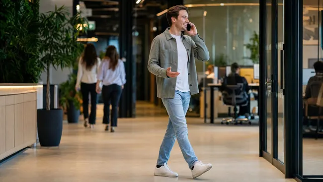 Korte lijnen en ruimte om je eigen aanpak neer te zetten. Man loopt bellend door een open kantoor