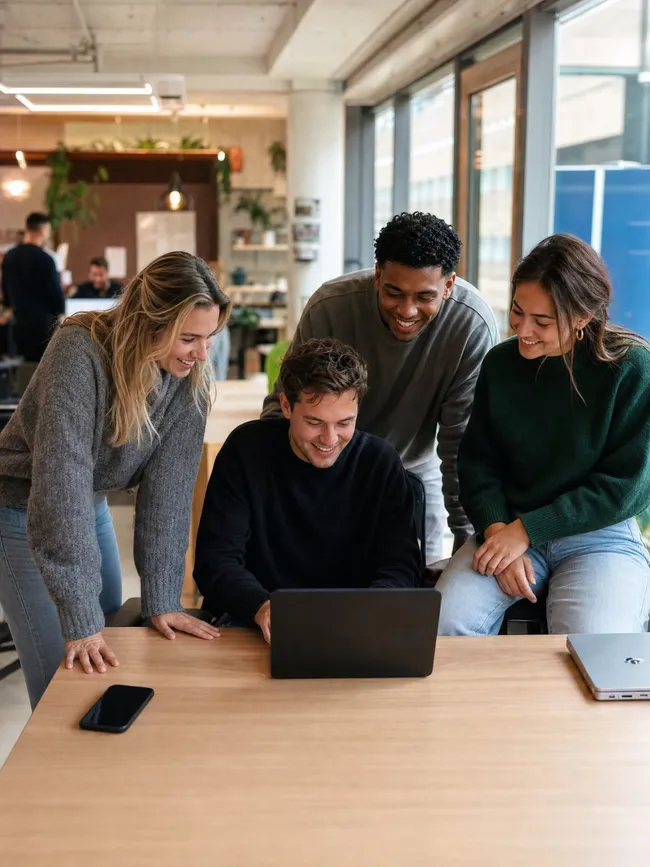 Vier successen en belangrijke momenten samen met het team. Vier collega's kijken samen naar een laptop aan een werktafel