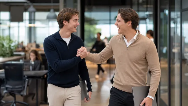Initiatief en resultaat blijven niet onopgemerkt. Goed werk krijgt waardering. Twee collega's geven elkaar een hand in een kantoorgang