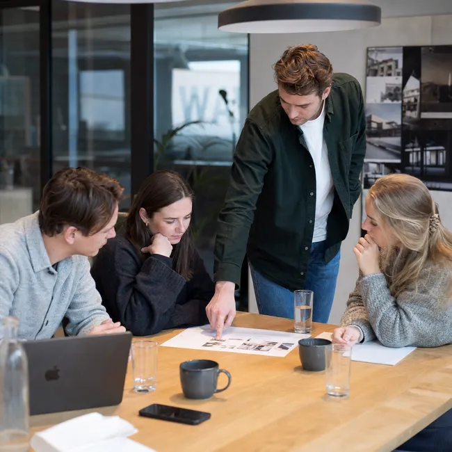 Persoonlijke aandacht in plaats van een nummer zijn Vier collega's overleggen aan een vergadertafel over uitgeprinte documenten